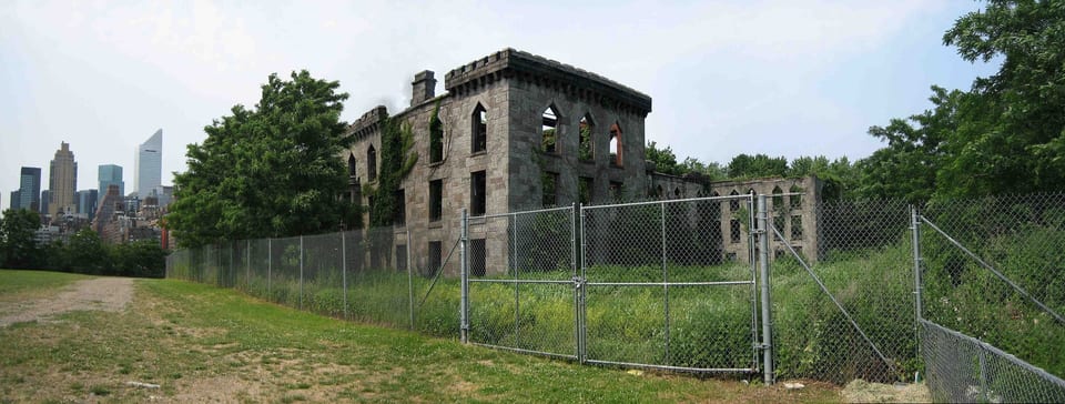 Panorama ruin neogotyckiego szpitala ospy na południowym krańcu Roosevelt Island, za nimi rzeka i wieżowce.