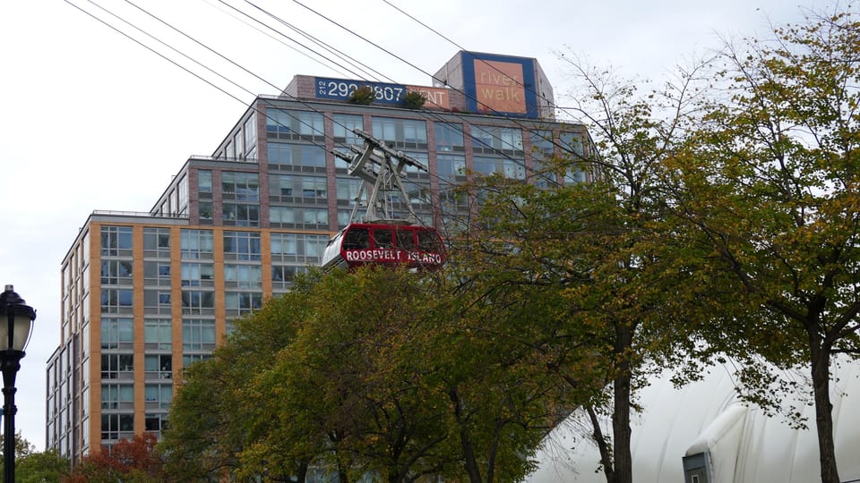 Czerwona kabina kolejki linowej Roosevelt Island Tramway nad East River, w tle most Queensboro.